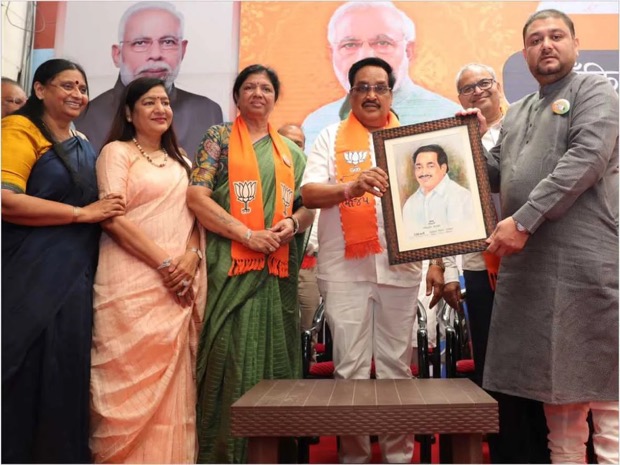 C. R. Patil on stage at a public event, receiving a framed portrait, with other participants beside him and a printed backdrop behind.