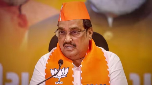 C. R. Patil speaking at a press briefing, wearing a ceremonial cap and stole, with microphones in front of him.