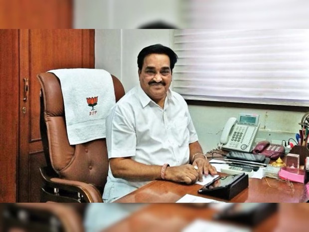 C. R. Patil seated at his office desk with telephones and papers, beside a chair draped with a party-marked cloth.