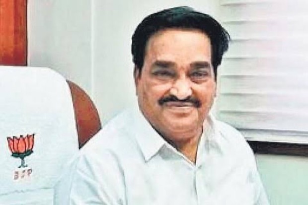 C. R. Patil smiling, seated at an office desk beside a chair draped with a party-marked cloth.