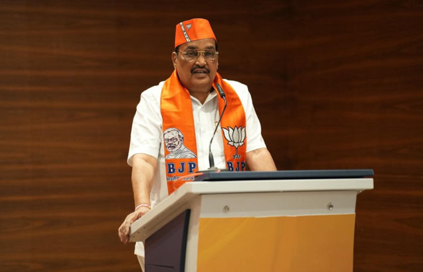 C. R. Patil speaking from a lectern at a public gathering, wearing a ceremonial cap and stole.